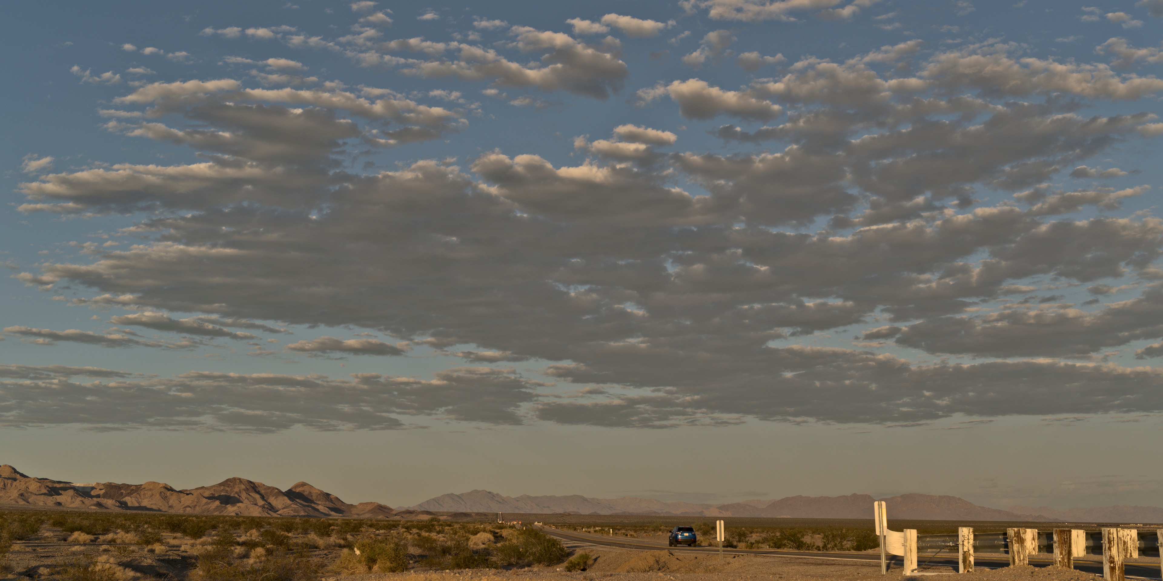 Cars heading west on Route 66 across the Mojave under a wide cloud-streaked sky