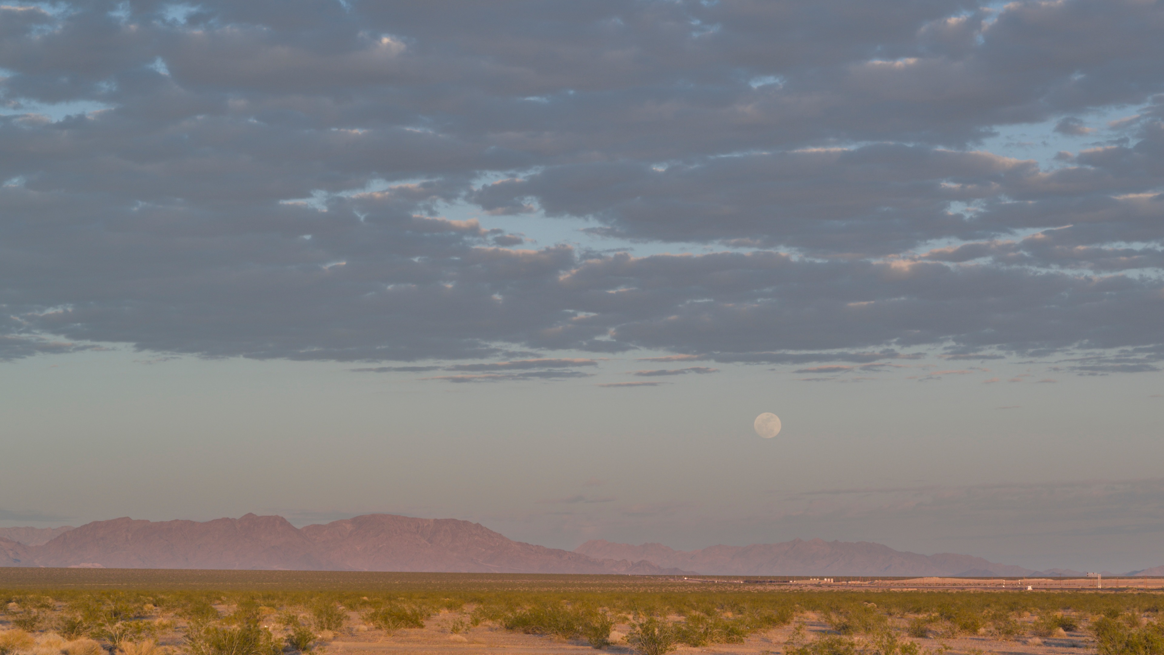 Full moon rising over distant mountains across the Mojave at dusk