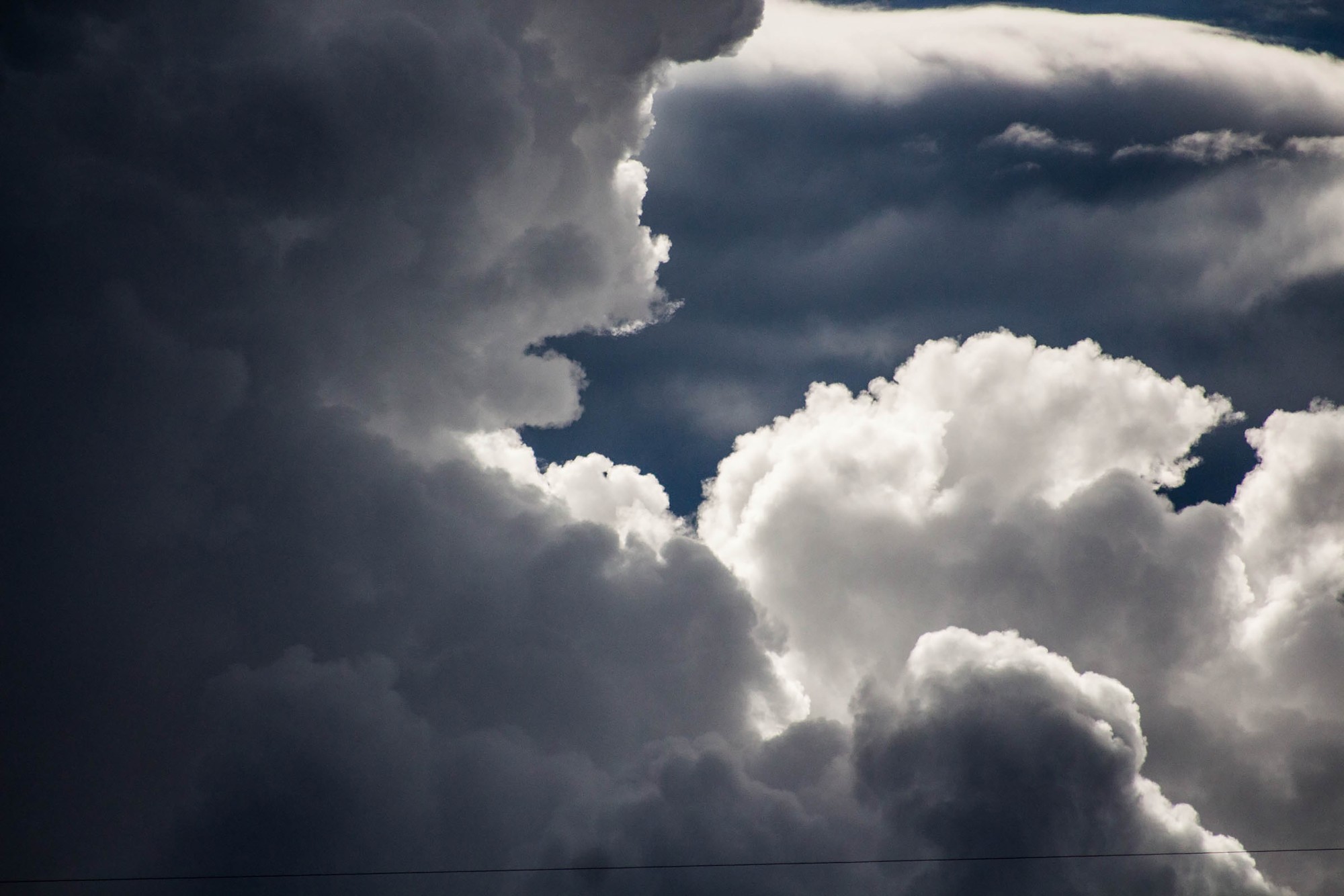 Towering storm clouds, dark on the left and sunlit white on the right, with a patch of deep blue sky between them